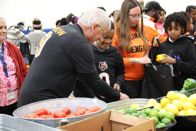 Jim Burrow placing fruit in a young boy's bag in a school gymnasium at a nonprofit event.