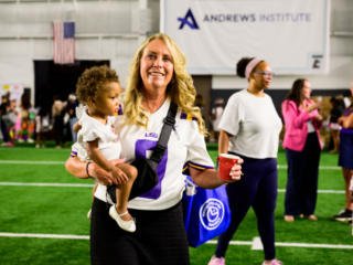 GS_0334 Robin Burrow smiling and holding a small child at The Joe Burrow Foundation's second-annual Burreaux's Back-to-School Kickoff.