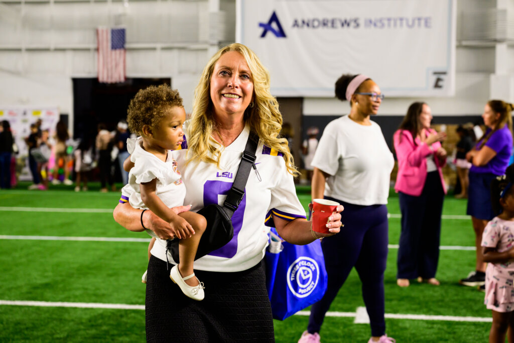 Robin Burrow smiling and holding a small child at The Joe Burrow Foundation's second-annual Burreaux's Back-to-School Kickoff.