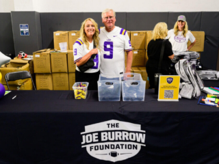 GS_0371 Robin and Jim Burrow hugging and smiling while standing behind a table at The Joe Burrow Foundation's second-annual Burreaux's Back-to-School Kickoff